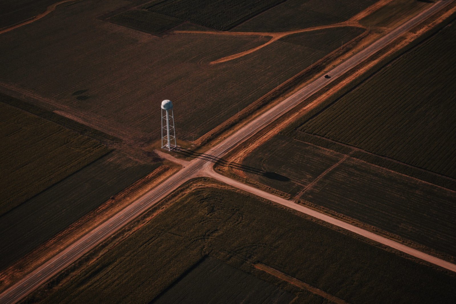 A beautiful aerial shot of narrow roads intersection in the countryside with a white tower in the middle